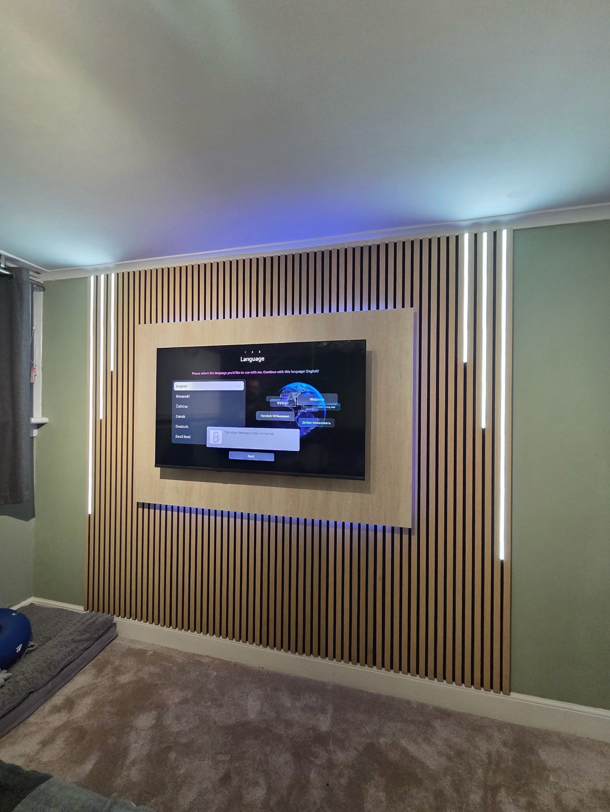 Modern home media room with flat-screen TV mounted on wood slat accent wall with LED lighting strips.