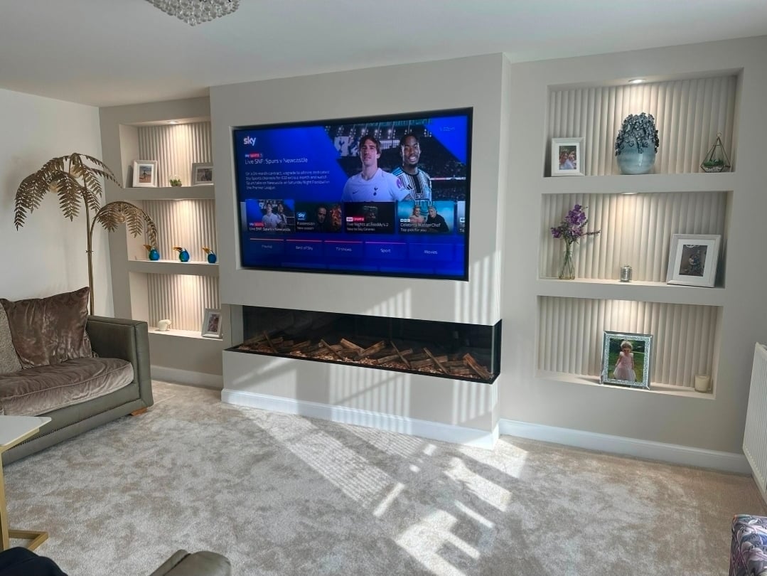 Modern living room with wall-mounted TV above fireplace, built-in shelving, decorative plants, and minimalist decor