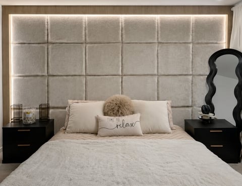 Modern bedroom with upholstered headboard, bed with decorative pillows and throw, black nightstands, and wavy wall mirror